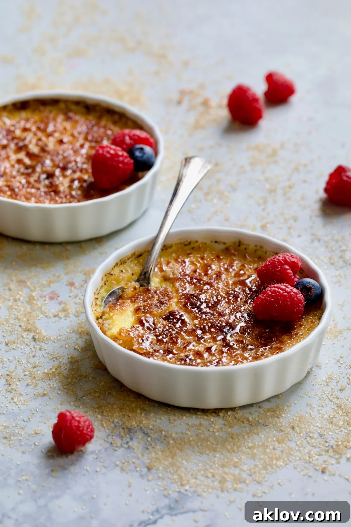 Two dishes of Classic Crème Brûlée for Two with turbinado sugar scattered over the surface, awaiting caramelization.