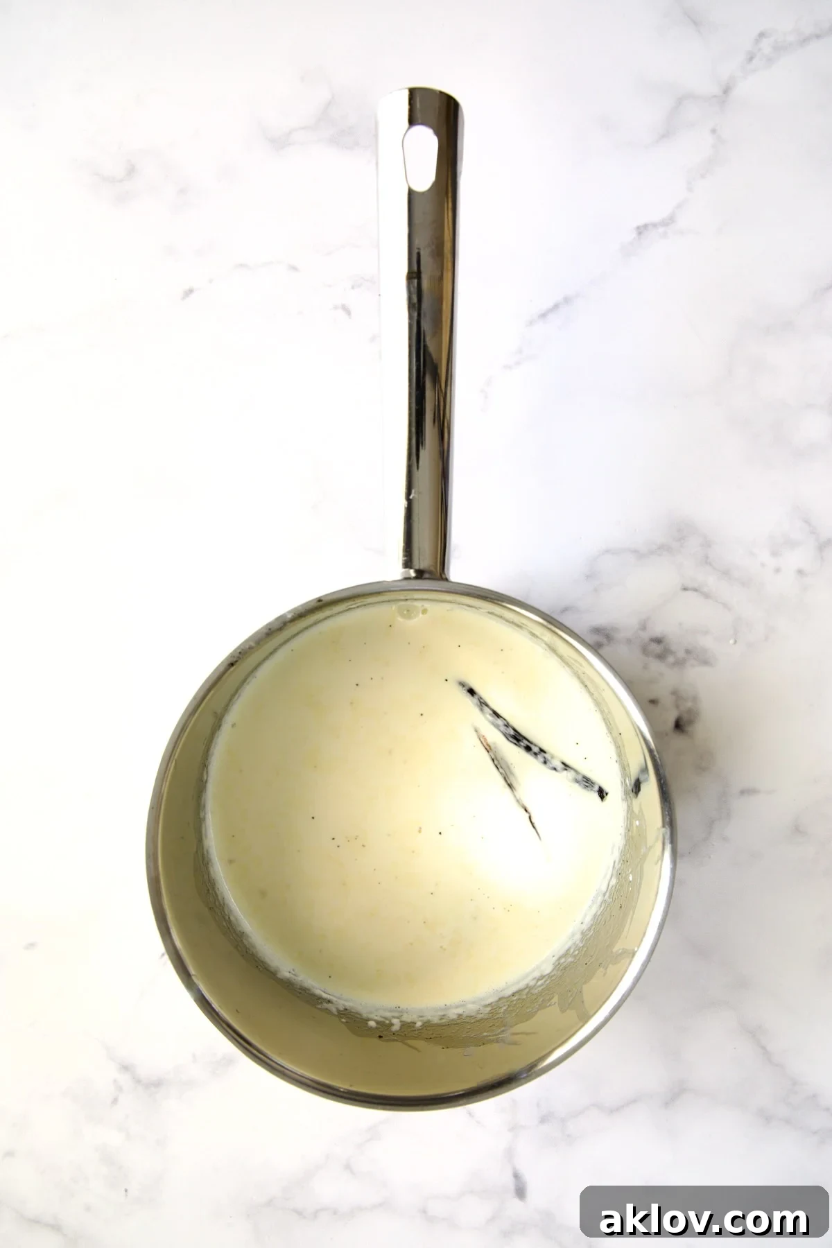 Heavy cream infused with a vanilla bean half gently simmering in a stainless steel saucepan, releasing its aromatic flavor.