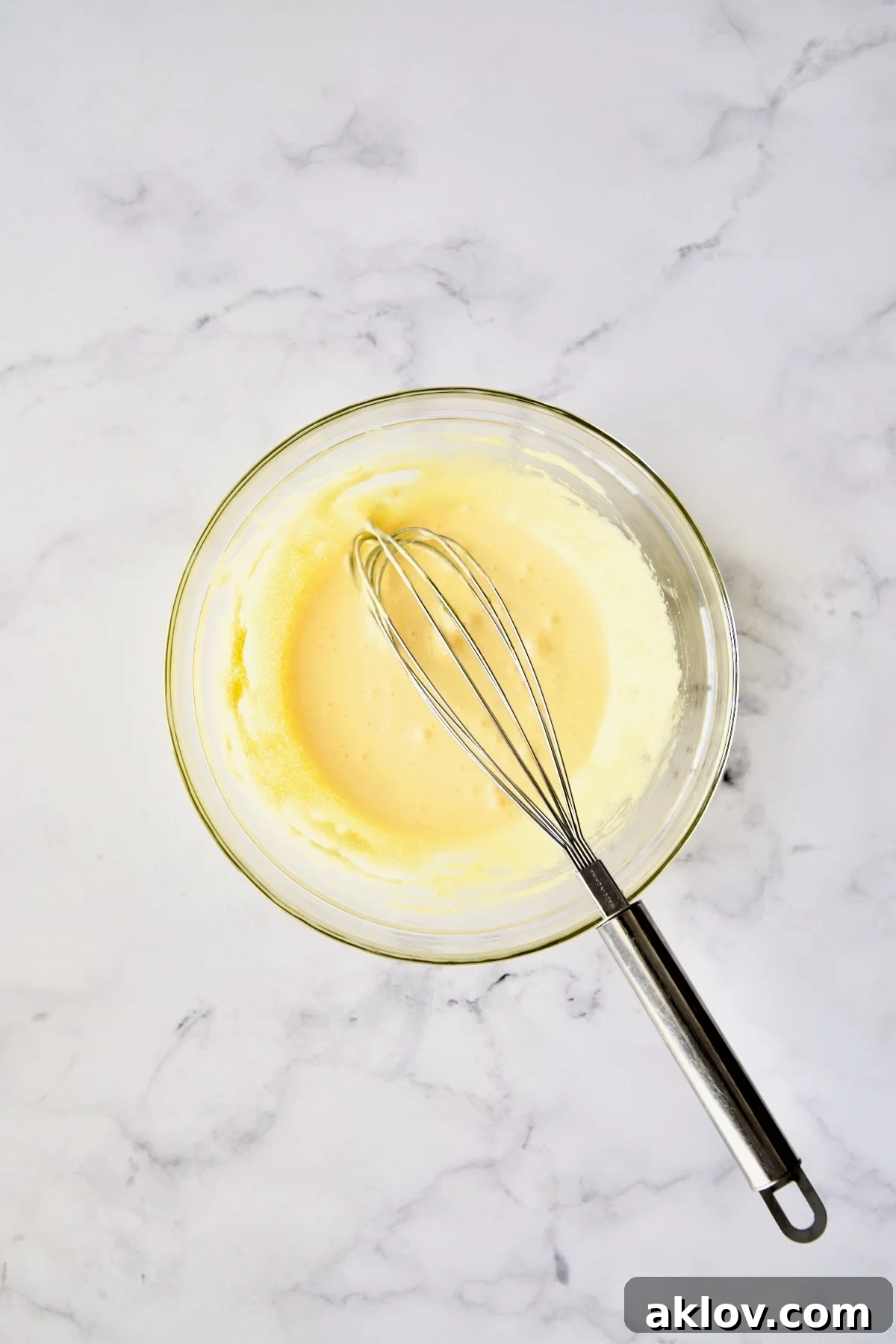 Egg yolks and sugar expertly whisked to a pale yellow and thick consistency in a clear glass bowl, ready for the next step.
