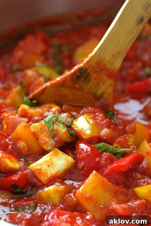 Close-up photo of vegetables being stirred in sauce with wooden spoon.