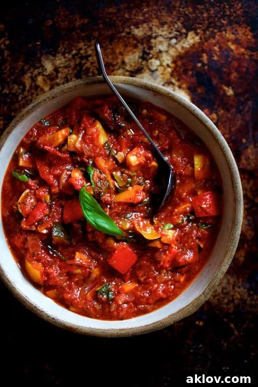 Photo of ratatouille in clay bowl with black serving spoon and garnished with fresh basil.