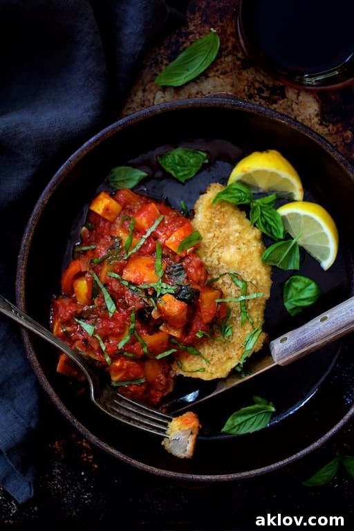 Photo of Chicken Scallopini with Roasted Vegetable Ratatouille in clay dish garnished with fresh basil and lemon wedges.