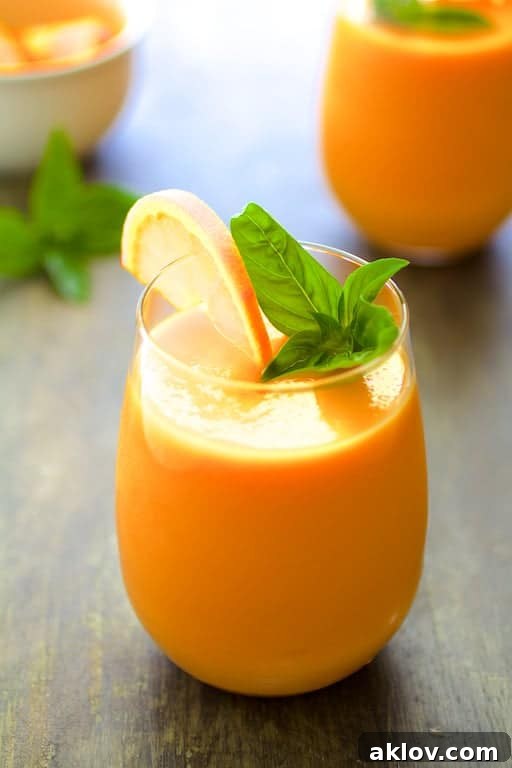 Chilled Cantaloupe Soup garnished with an orange wedge and fresh basil.