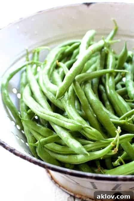 A pristine antique white colander overflowing with freshly picked, vibrant green beans, ready for preparation.