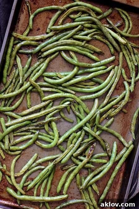 A baking sheet filled with perfectly roasted green beans, showing tender-crisp texture and subtle charring, straight from the oven.
