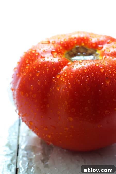A close-up photograph of a vibrant, freshly washed tomato, glistening and ready for chopping.