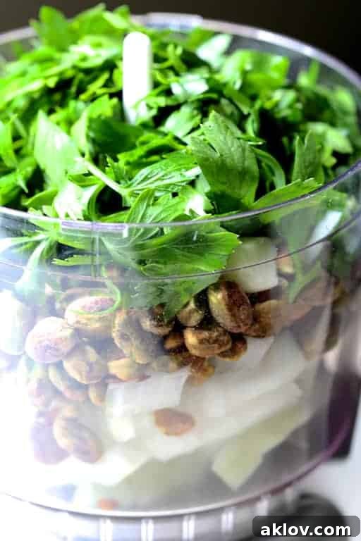 Photo of ingredients for meatballs in mini food processor before blending, showcasing fresh herbs and nuts.