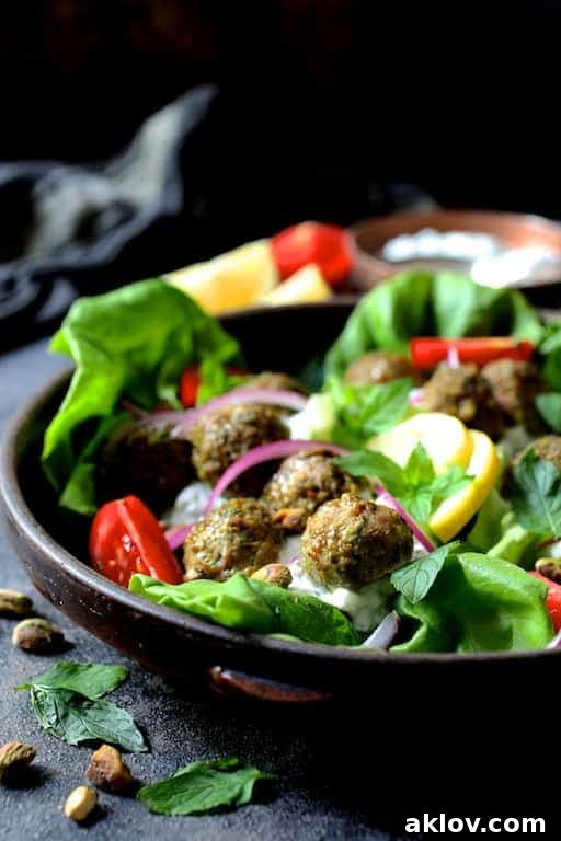 Photo of Turkish Turkey Meatball Lettuce Wraps with Tzatziki in clay dish with all the garnishes: Tomatoes, onion slices, lemon wedges, pistachios, mint leaves.