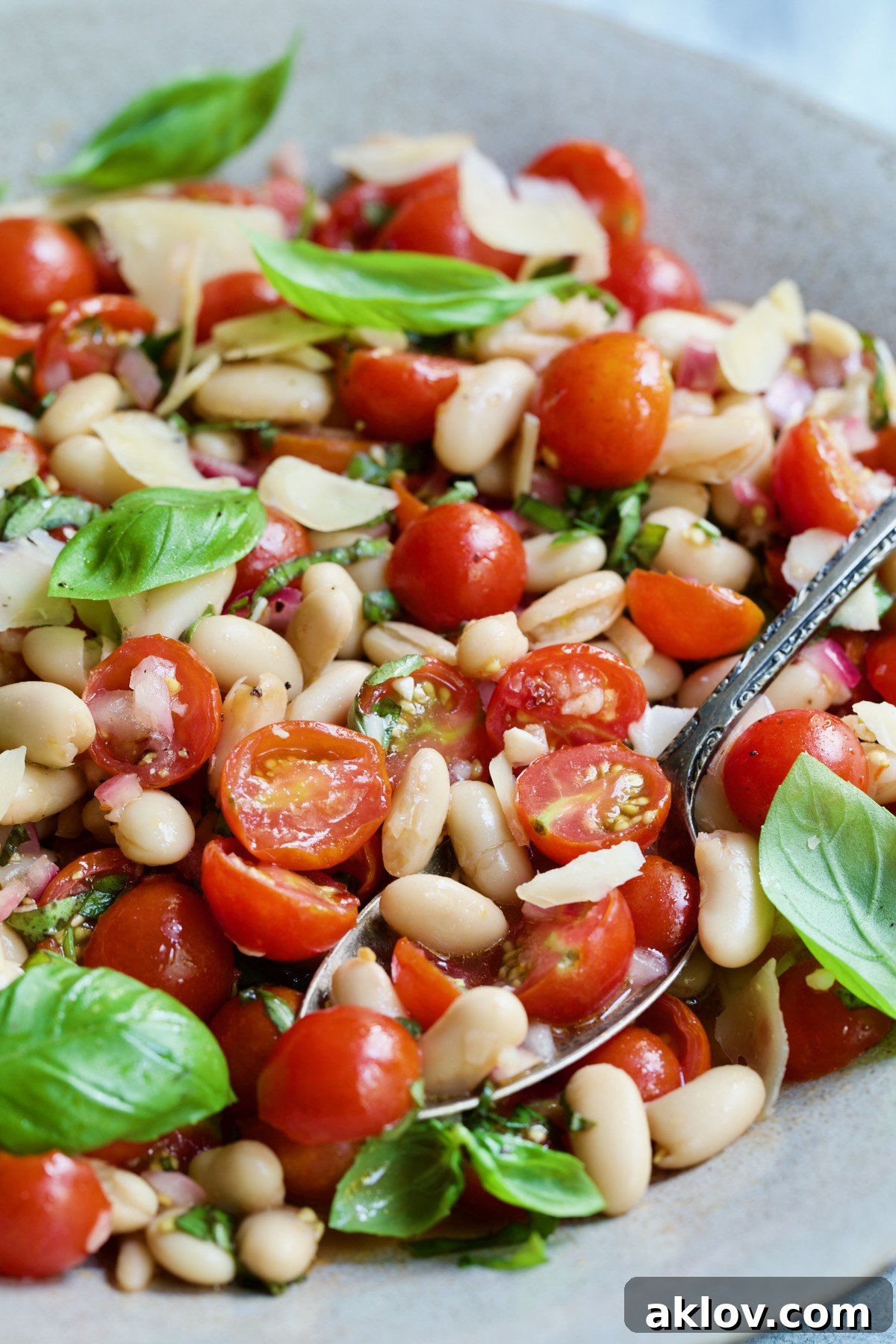 A serving spoon lifting a portion of Tuscan Cherry Tomato and White Bean Salad from a bowl, highlighting its fresh ingredients.