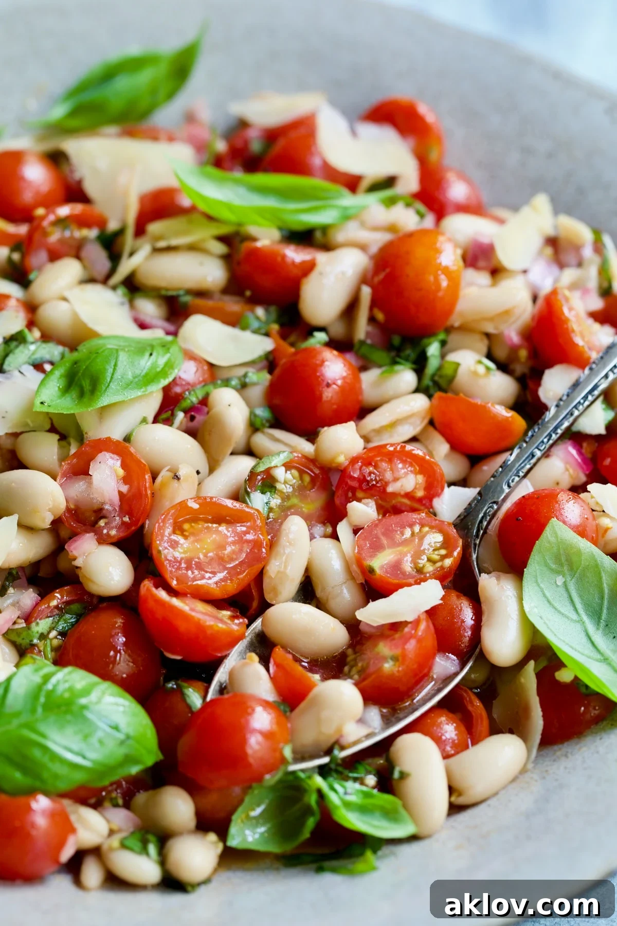 A serving spoon lifting a generous portion of Tuscan Cherry Tomato and White Bean Salad, showcasing the vibrant colors and fresh ingredients.