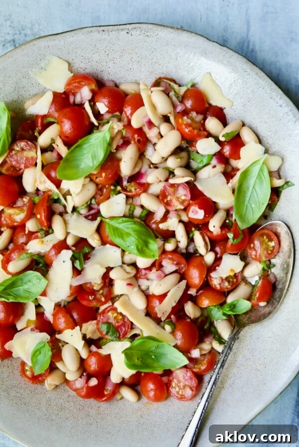 Tuscan Cherry Tomato and White Bean Salad in a serving bowl with a spoon, garnished with fresh basil.