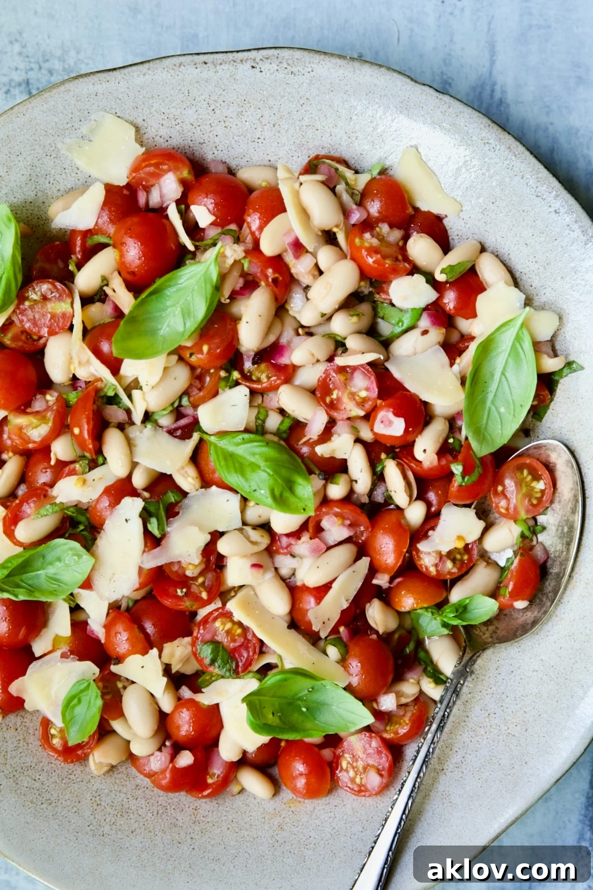 A top-down view of Tuscan Cherry Tomato and White Bean Salad in a rustic serving bowl, accompanied by a wooden serving spoon.