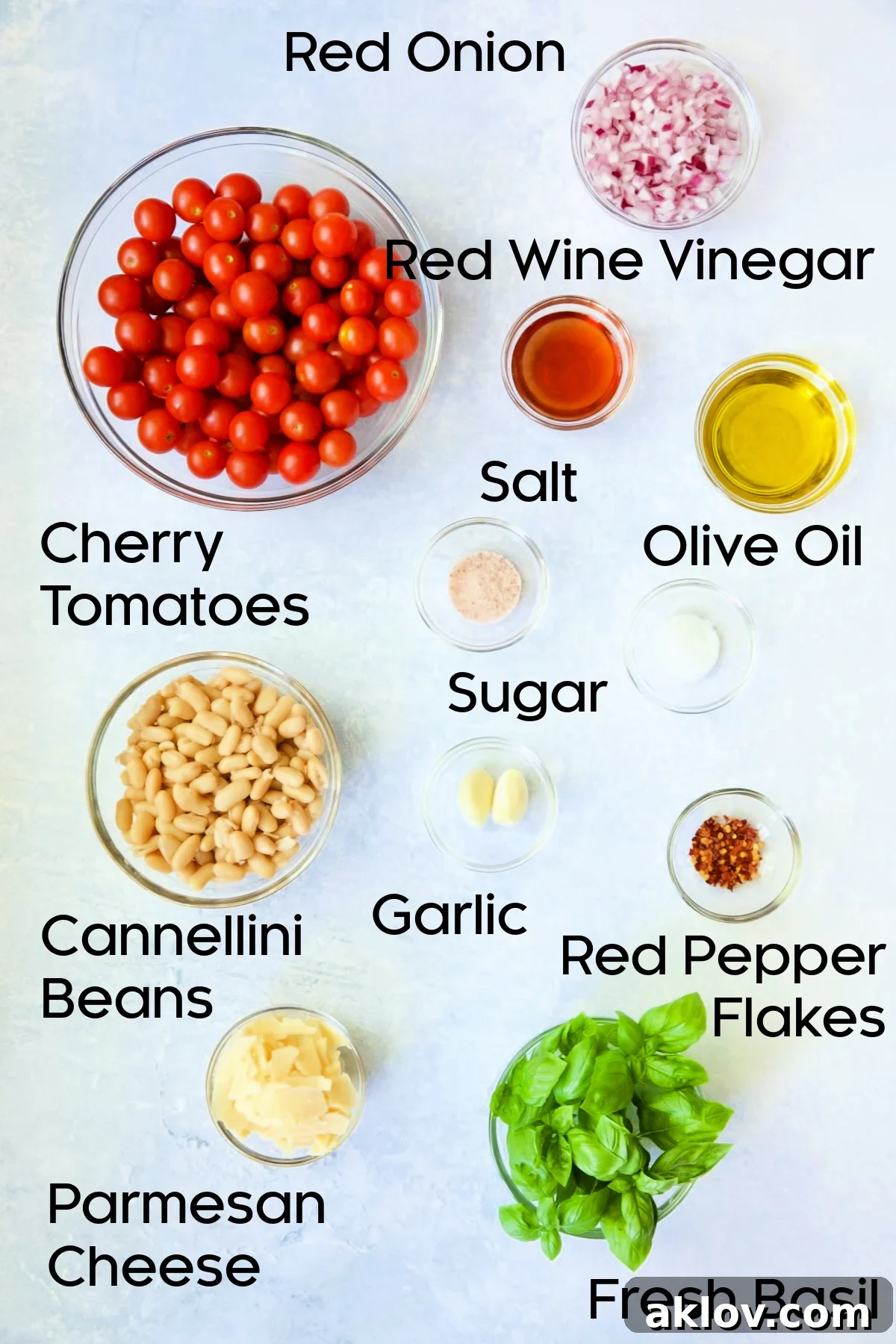 Individual glass bowls showcasing the fresh ingredients for Tuscan Cherry Tomato and White Bean Salad: halved cherry tomatoes, red onion, basil, and cannellini beans.