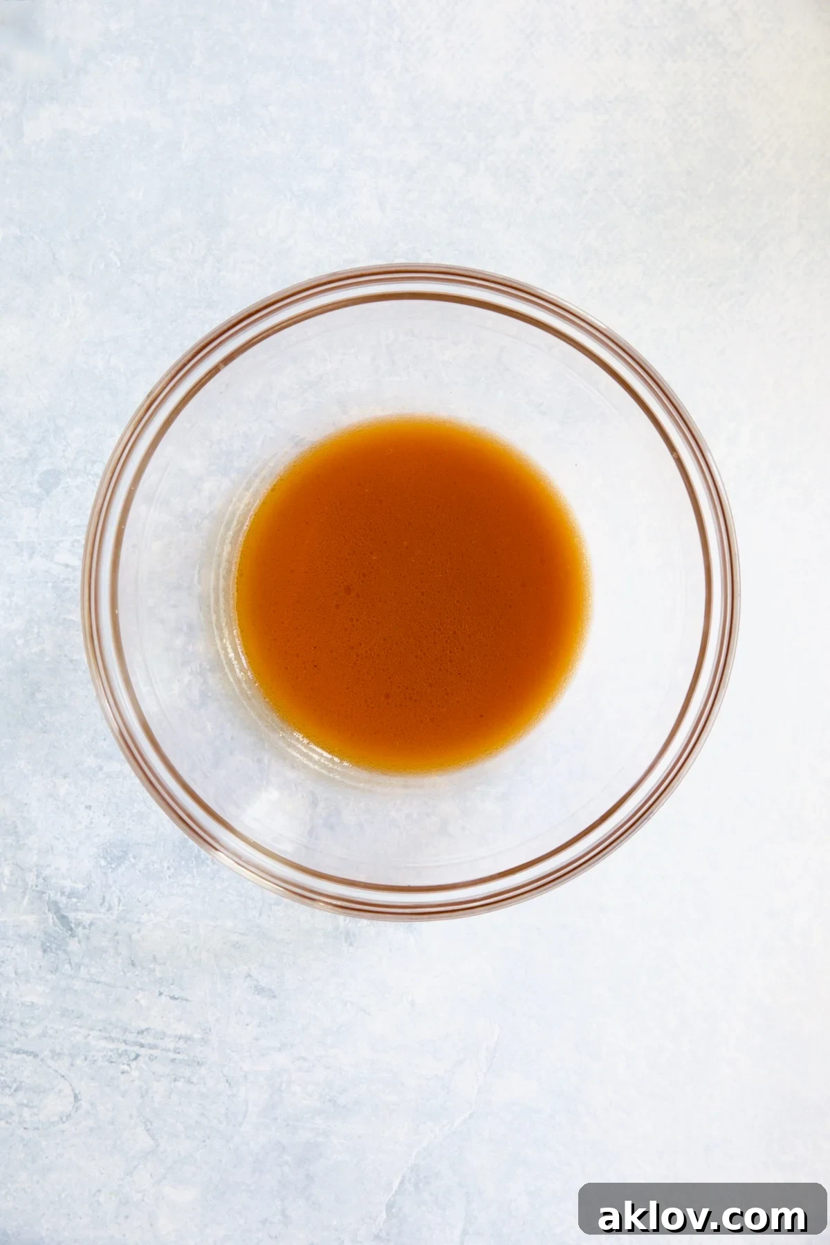 A glass bowl containing the freshly prepared salad dressing, a blend of reserved tomato juices, red wine vinegar, olive oil, garlic, and red pepper flakes.