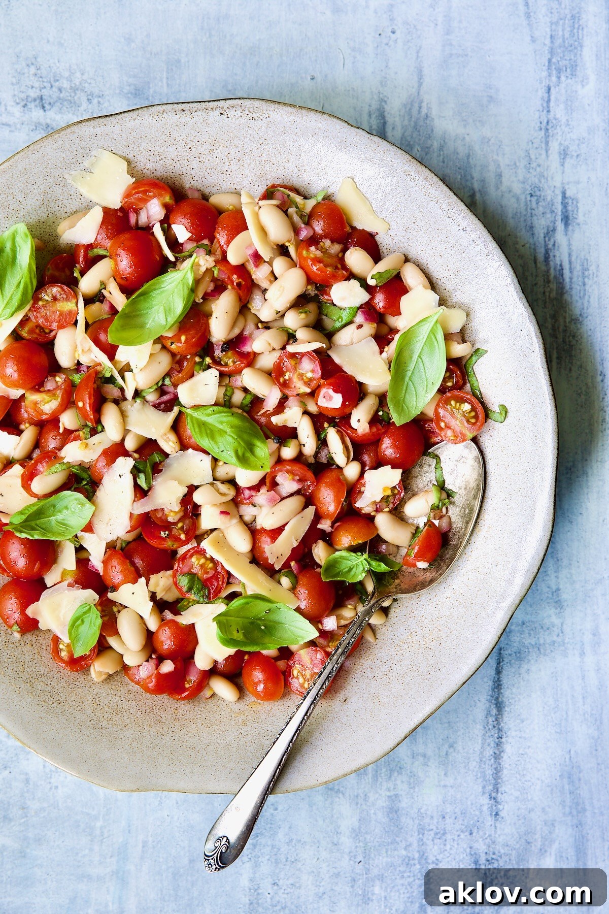 A beautifully presented Tuscan Cherry Tomato and White Bean Salad in a serving bowl, garnished with fresh basil, with a serving spoon tucked in.