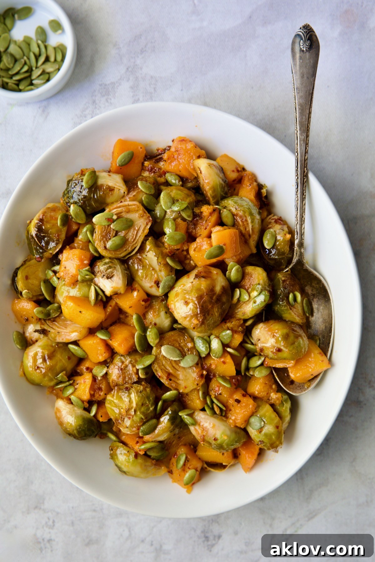 The completed Maple Chili Crisp Brussels Sprouts and Butternut Squash, beautifully plated and garnished with pepitas, ready to be enjoyed from a white serving bowl with a spoon.