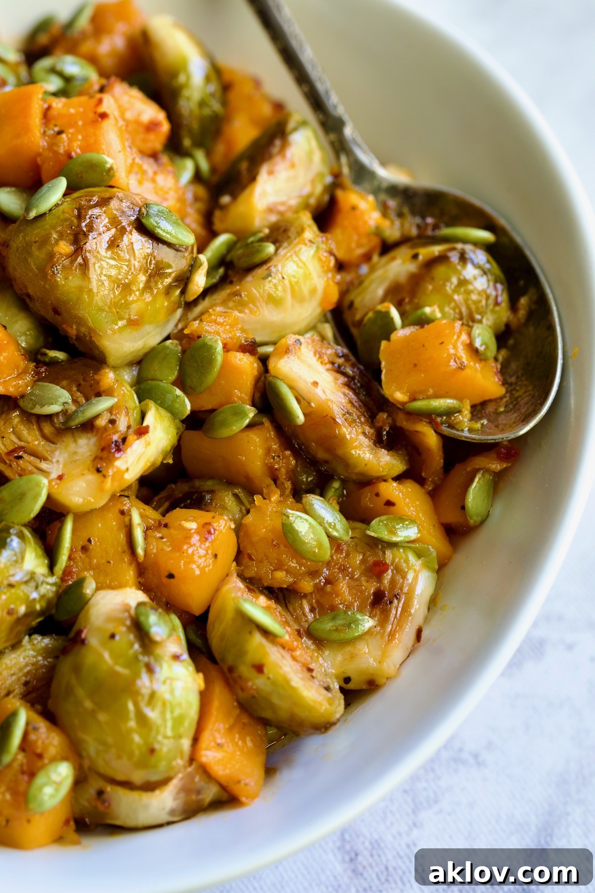 An inviting overhead shot of Maple Chili Crisp Brussels Sprouts and Butternut Squash, beautifully plated in a white serving bowl, garnished with crunchy pepitas, ready to be served.