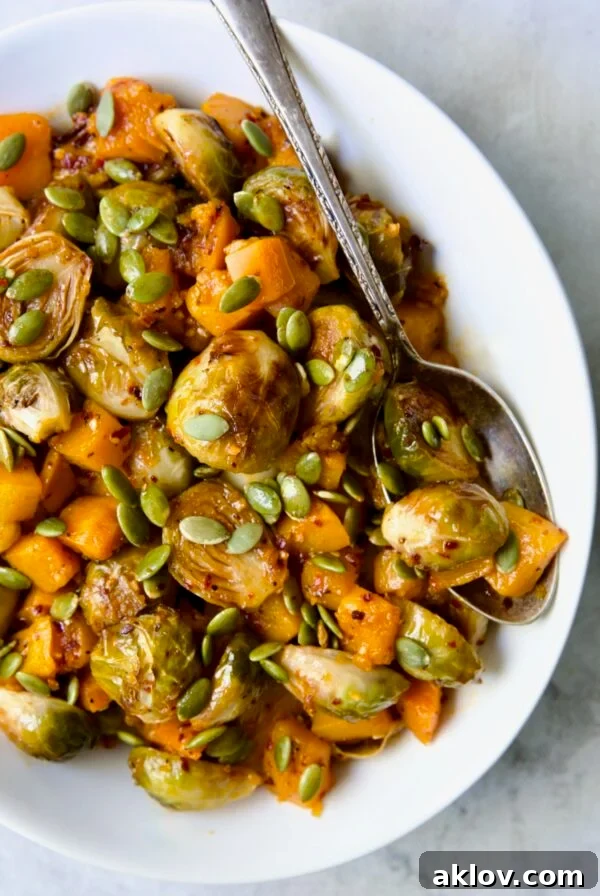 Maple Chili Crisp Brussels Sprouts and Butternut Squash garnished with pepitas in white bowl with serving spoon.