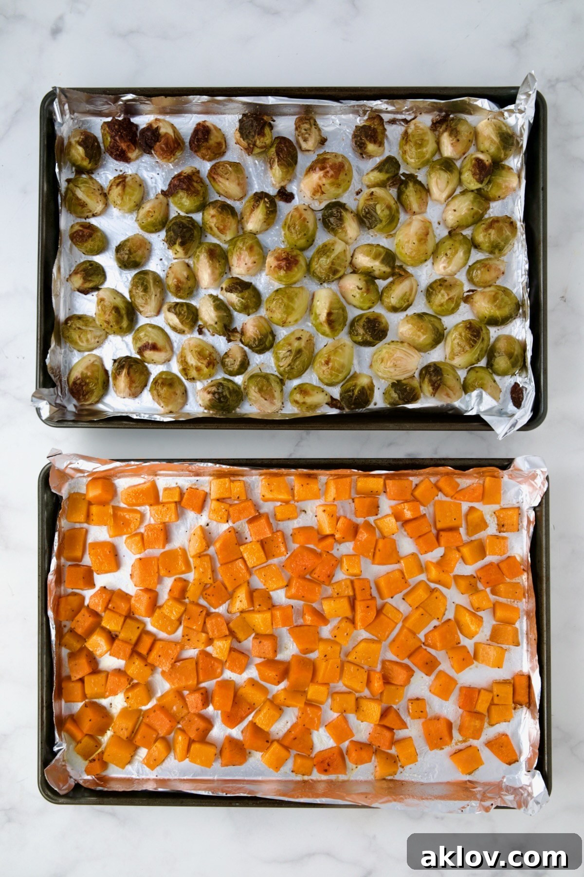 Golden-brown, roasted Brussels sprouts and tender, caramelized butternut squash are shown on their respective nonstick aluminum foil-lined rimmed baking sheets, having just emerged from the oven.