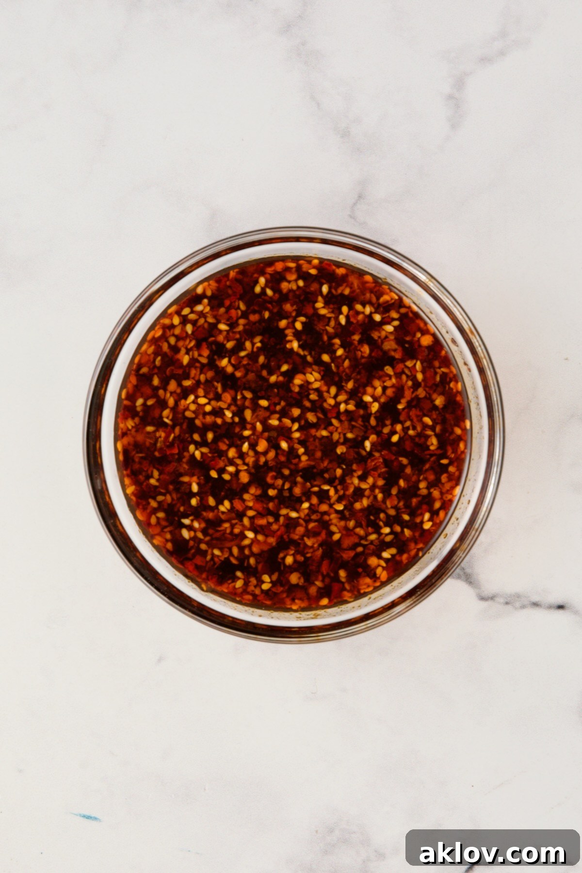 A small glass bowl holds the perfectly blended sauce for Maple Chili Crisp Brussels Sprouts and Butternut Squash, a vibrant mixture of maple syrup, chili crisp, and soy sauce.
