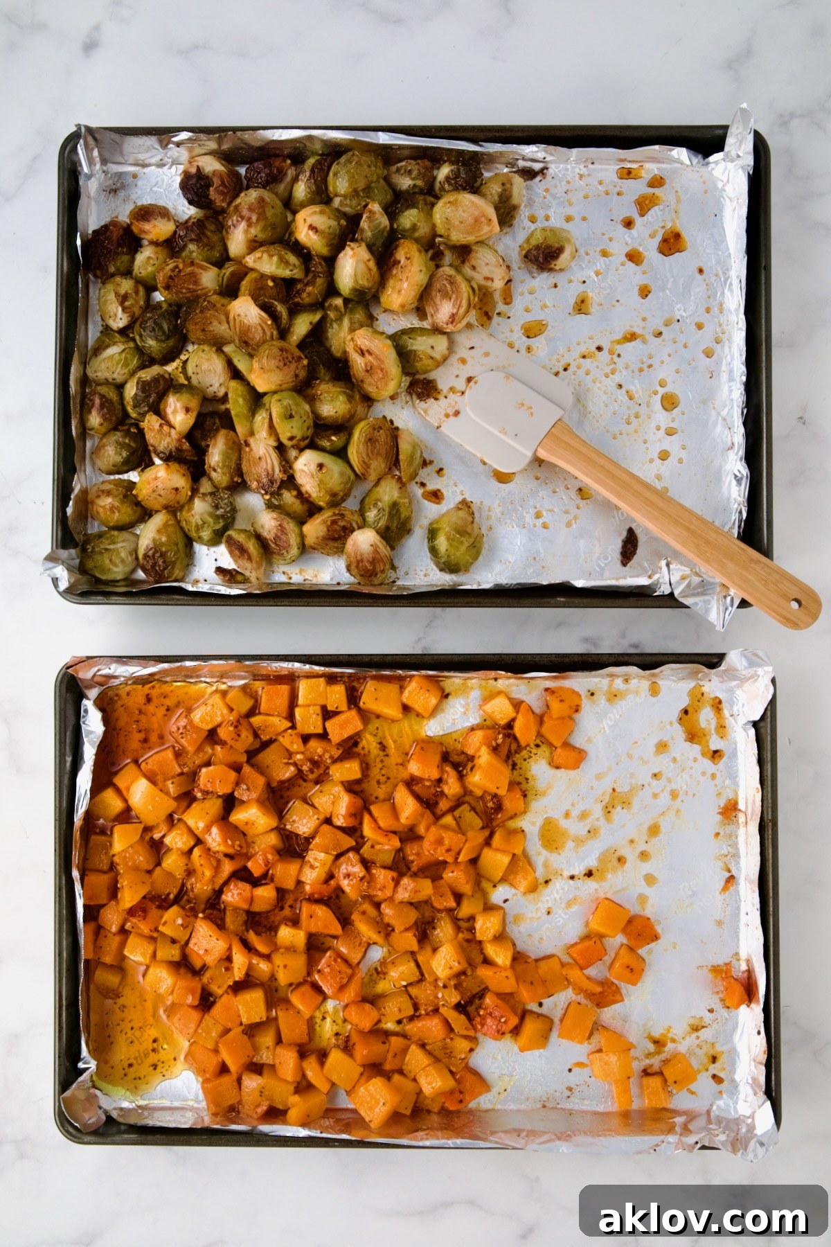 A wooden spatula gently stirs the roasted Brussels sprouts and butternut squash on a foil-lined baking sheet, ensuring the delicious sauce evenly coats every piece.