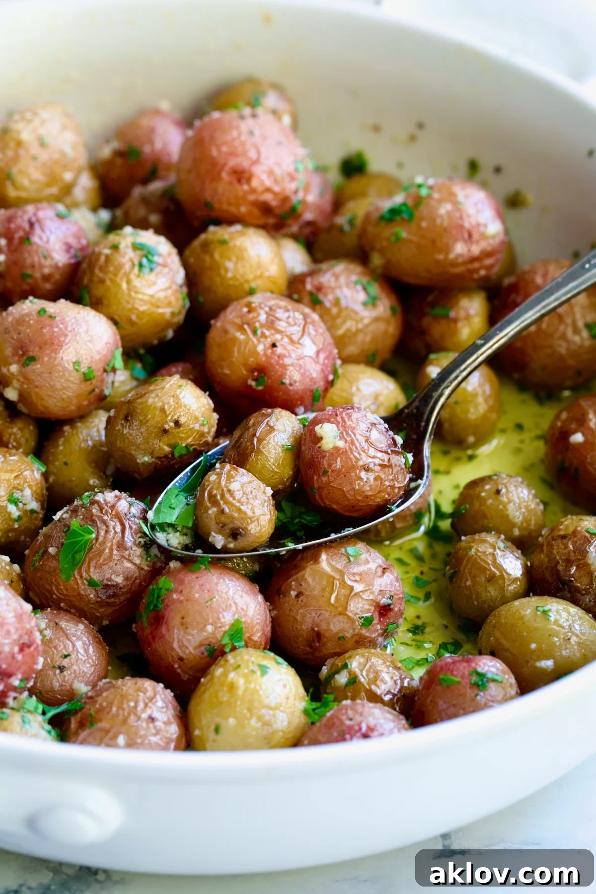 Garlic Butter Parmesan Mini Potatoes in round white baking dish with three on a serving spoon.