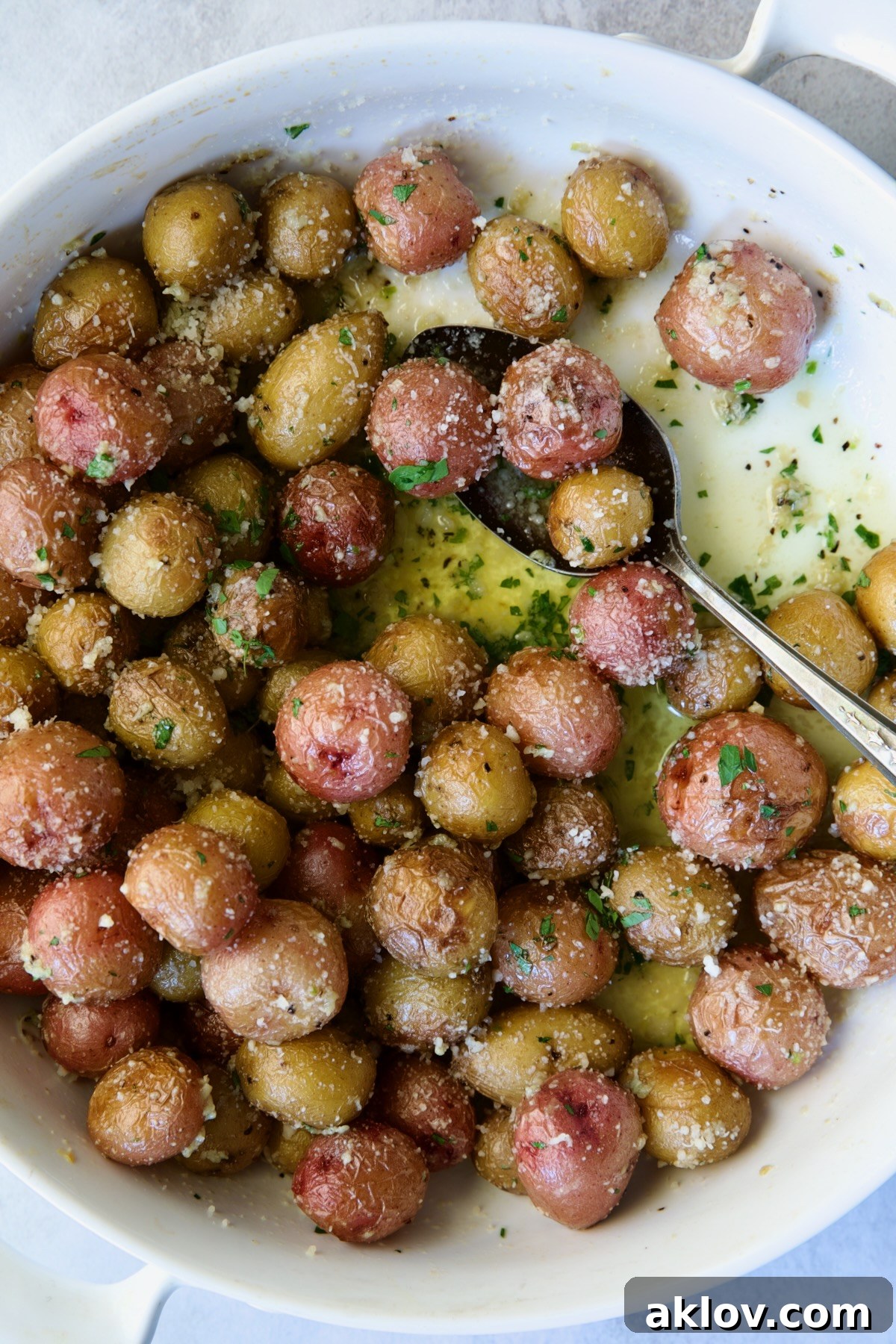 Garlic Butter Parmesan Mini Potatoes in round white baking dish with serving spoon.