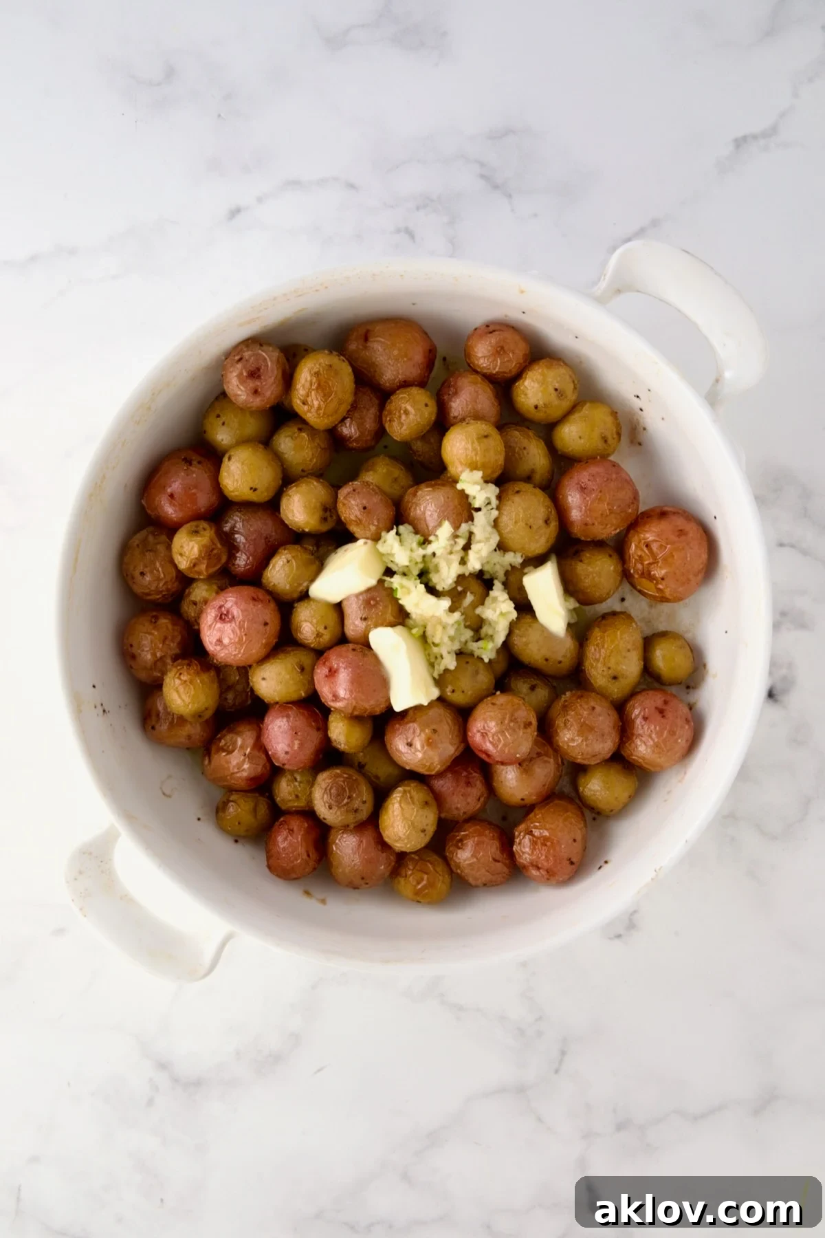 Butter and garlic added to roasted mini potatoes in round white baking dish.