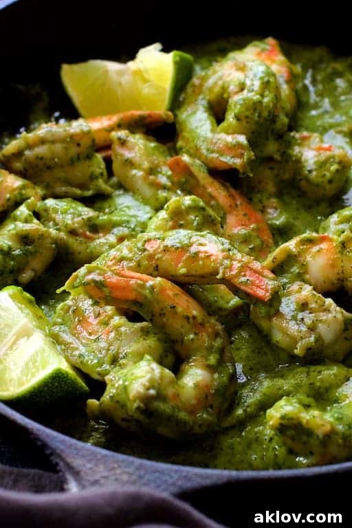 Close-up view of perfectly cooked shrimp submerged in creamy, bright green avocado butter, garnished with fresh lime wedges.