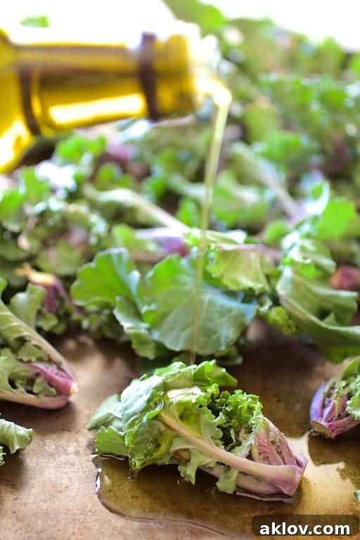 Crispy Balsamic Parmesan Kale Sprouts 3 Kale sprouts being drizzled with olive oil and balsamic vinegar on a baking sheet before roasting.