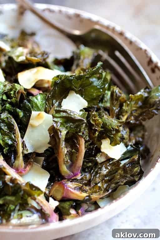 Crispy Balsamic Parmesan Kale Sprouts 5 Close-up of roasted kale sprouts generously topped with shaved Parmesan cheese in a white distressed bowl.