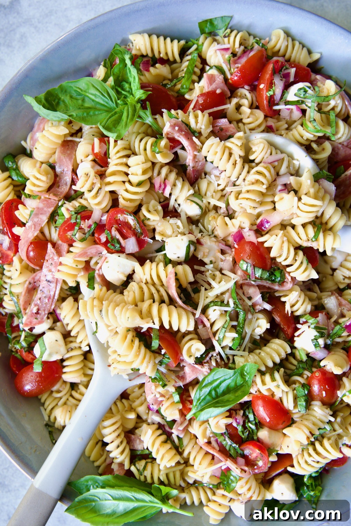 Caprese Pasta Salad in blue bowl being stirred with serving utensils.