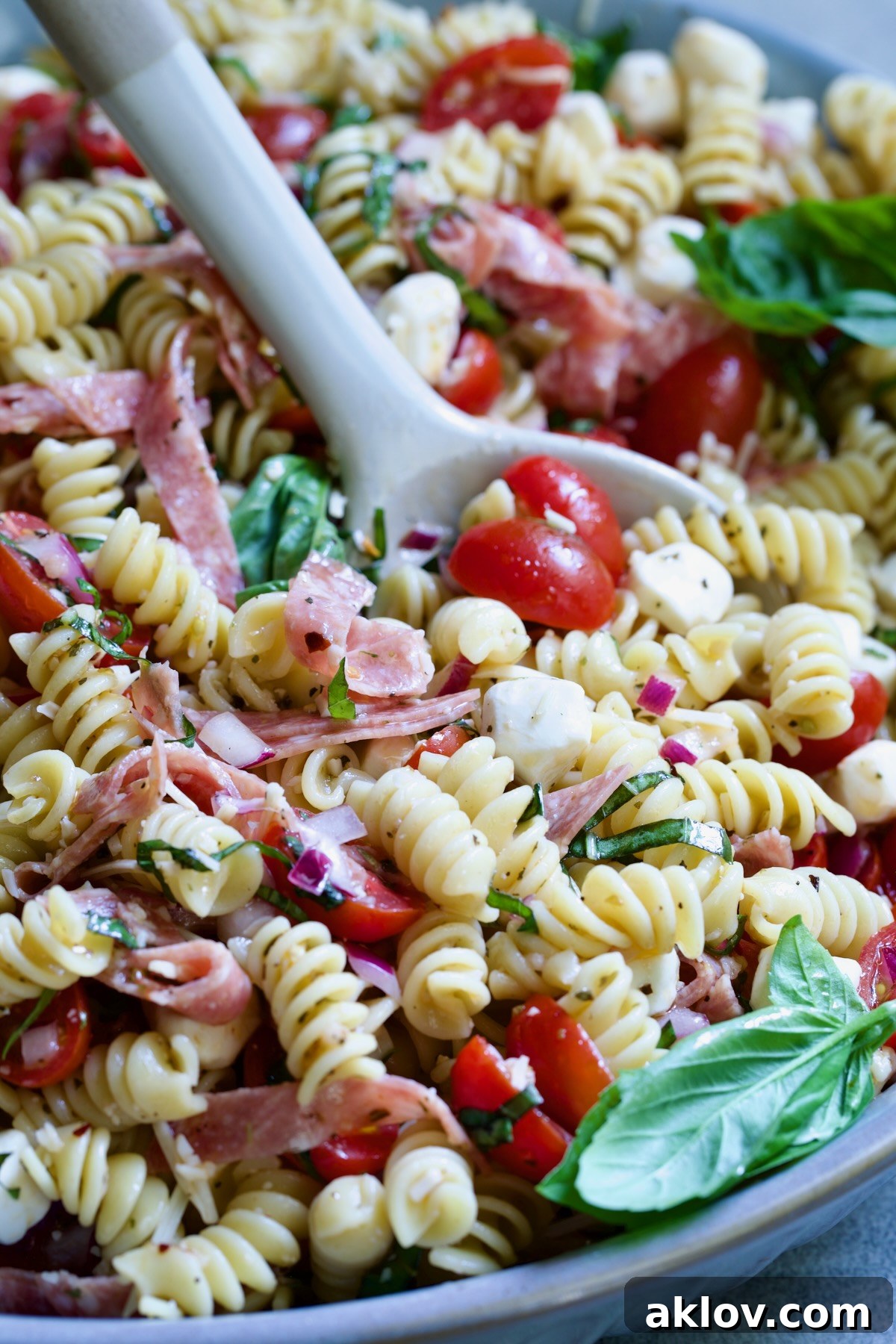 Caprese Pasta Salad in blue bowl being stirred with serving utensil.