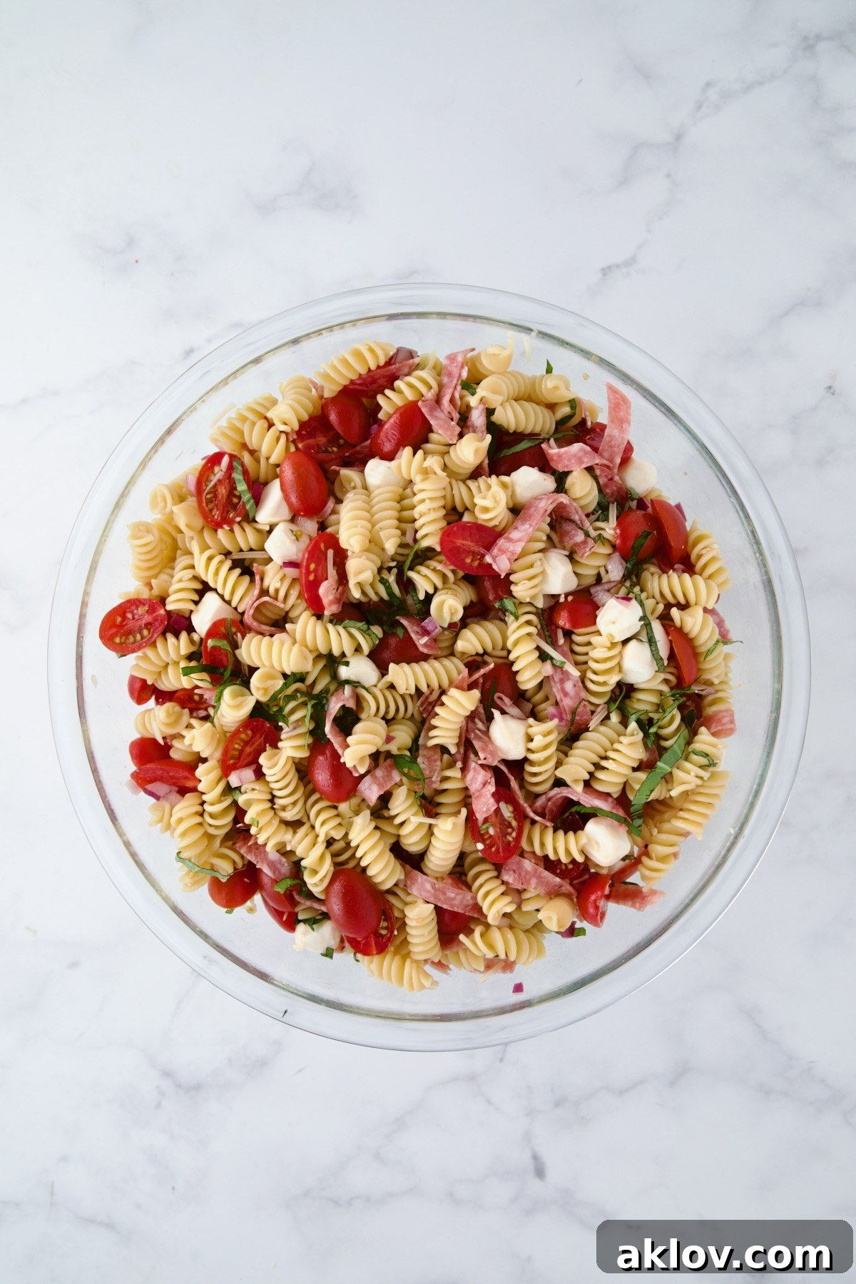 Ingredients for Caprese Pasta Salad in glass bowl after being stirred together.