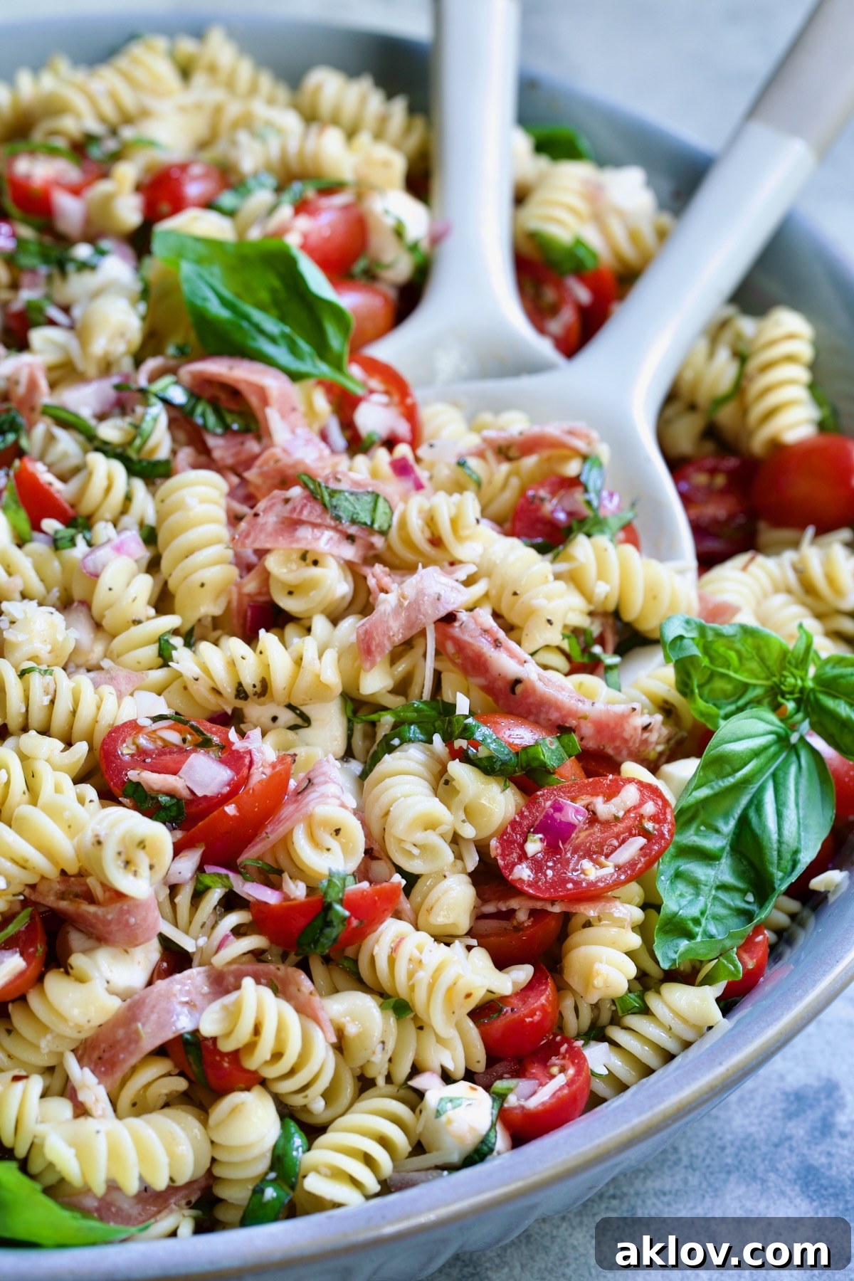 Caprese Pasta Salad in blue bowl being stirred with serving utensils.