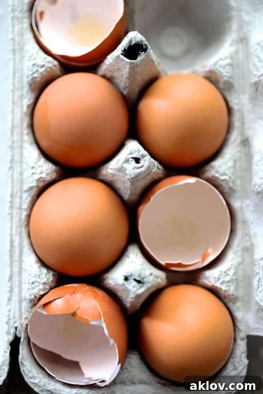 Photo of seven fresh brown eggs in a carton, with four whole eggs and three empty shells, essential for a rich strata.