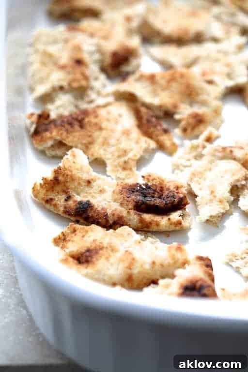 Process photo of the first layer of torn naan pieces arranged at the bottom of a white baking dish.