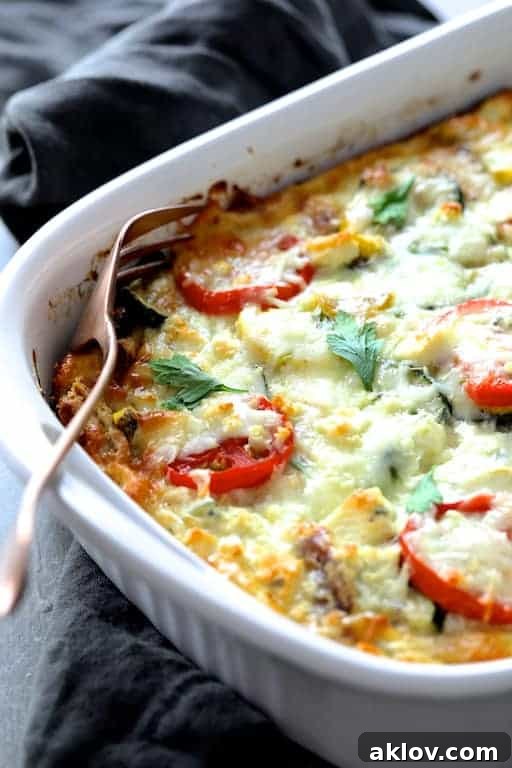 Photo of a baked Four Cheese Strata with Zucchini and Tomatoes placed on a gray towel, with a serving fork ready to dish out.