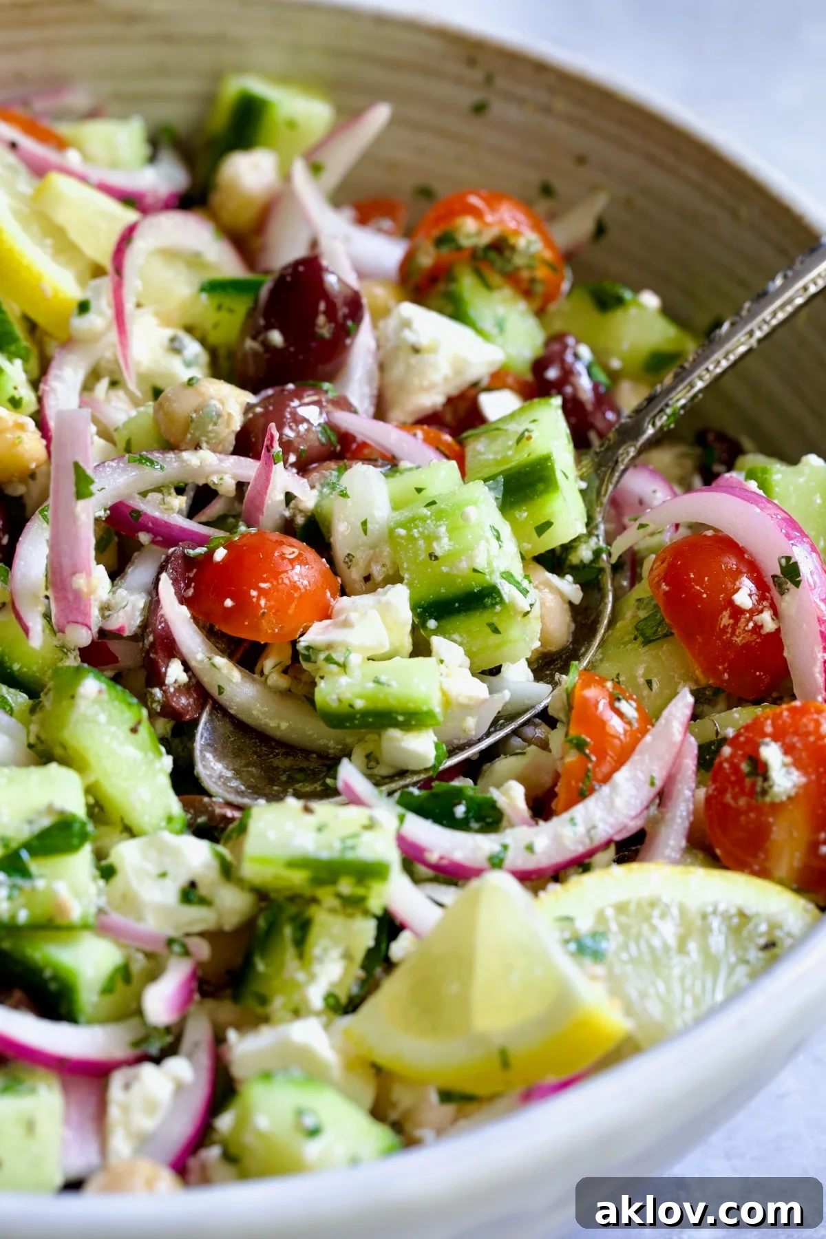 Greek Cucumber Salad in white bowl garnished with fresh lemon wedges.