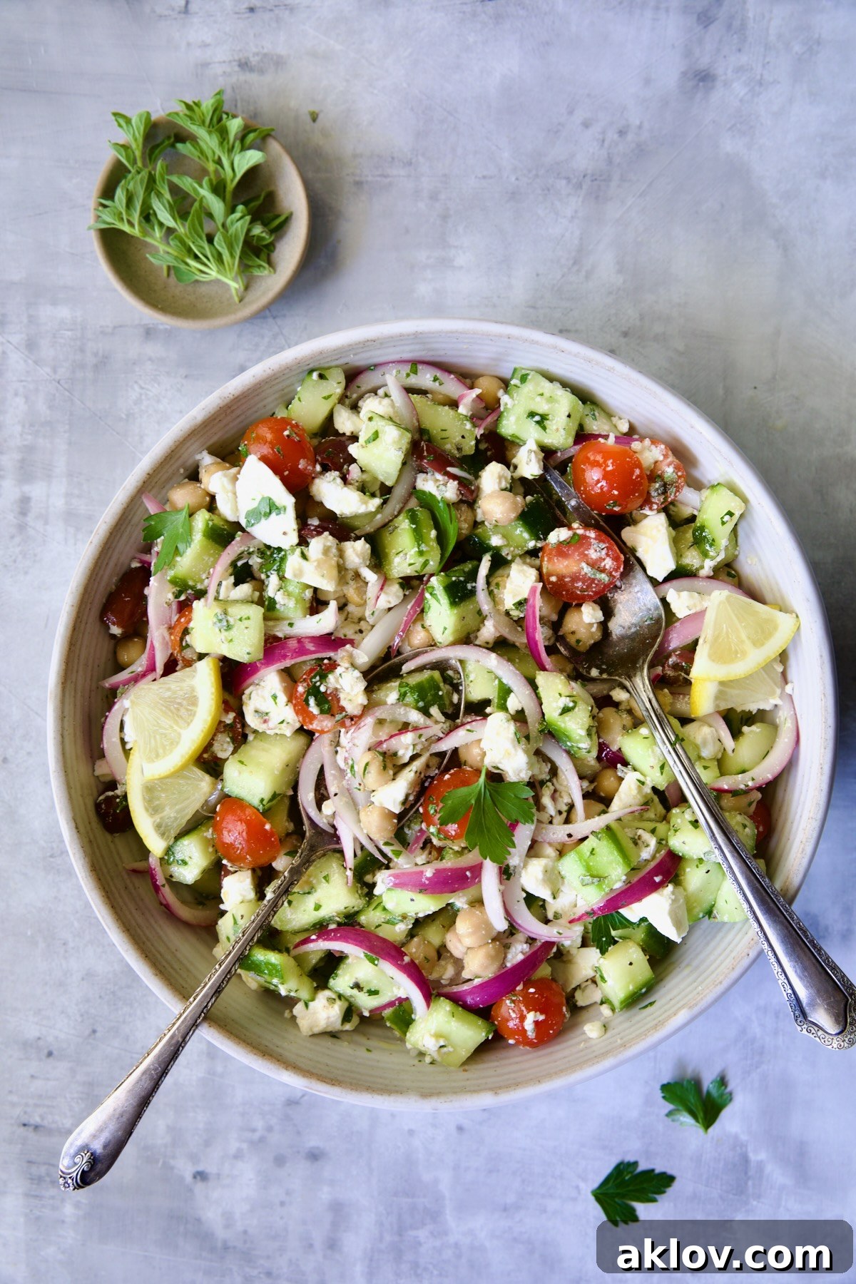 Greek Cucumber Salad in white serving bowl with serving utensils.