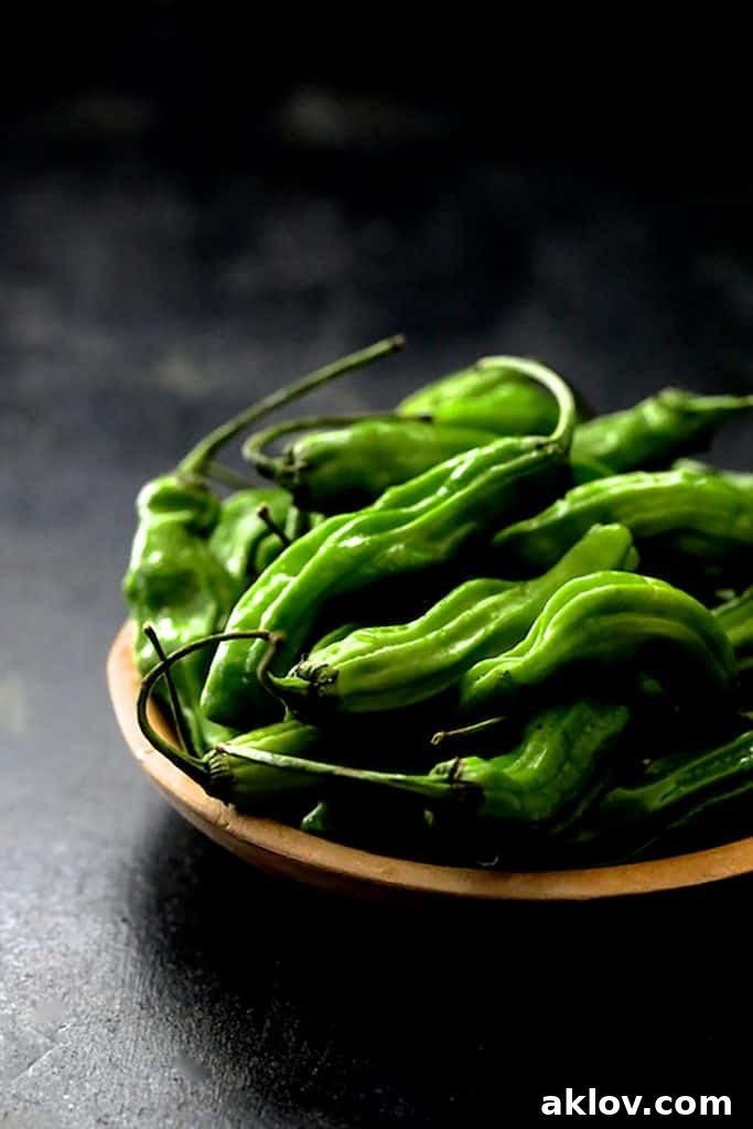 Fresh, uncooked shishito peppers resting in a rustic wooden bowl on a dark gray background, ready for cooking.