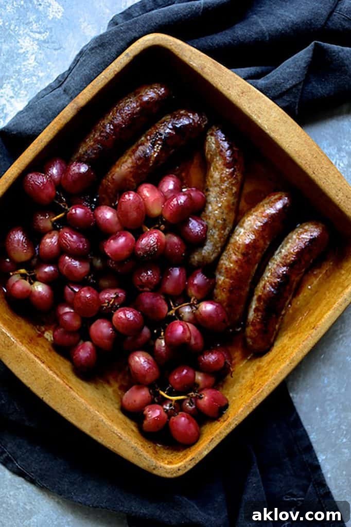 Photo of grapes and sausages in clay baking dish on dark gray towel.