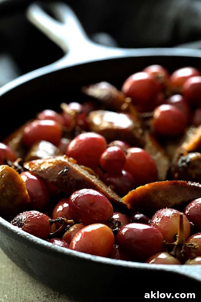 Photo of sliced sausages and grapes in cast iron skillet.