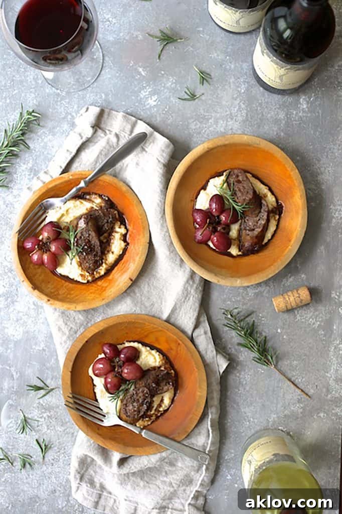Photo of three servings of Balsamic Italian Sausage and Grapes over Goat Cheese Polenta on light gray background with gray napkin, wine bottles and glass of wine garnished with rosemary.
