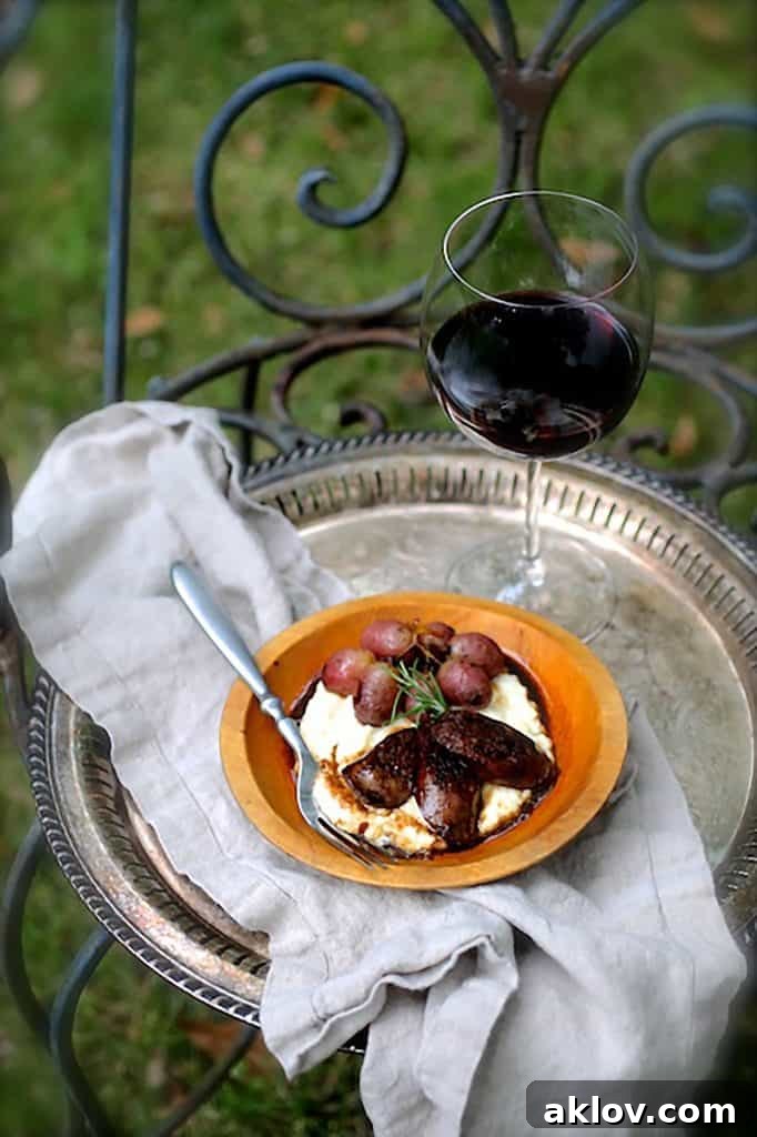 Photo of Balsamic Italian Sausage and Grapes over Goat Cheese Polenta on silver tray with glass of red wine on wrought iron chair.