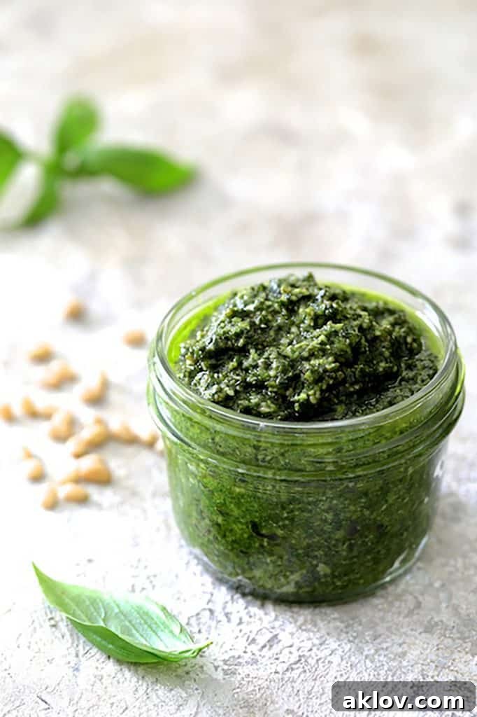 A pint-sized Mason jar filled with freshly made vibrant green pesto, set against a clean white background.