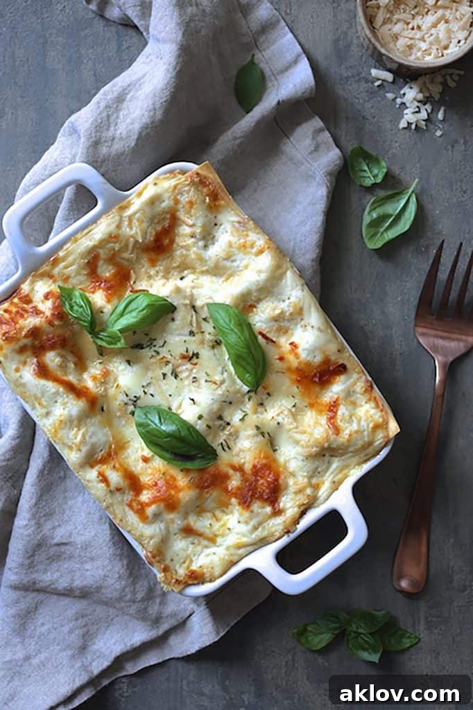 A serving of Lasagna with Pesto Green Beans and Potatoes, garnished with fresh basil, presented on a gray background with a serving fork.
