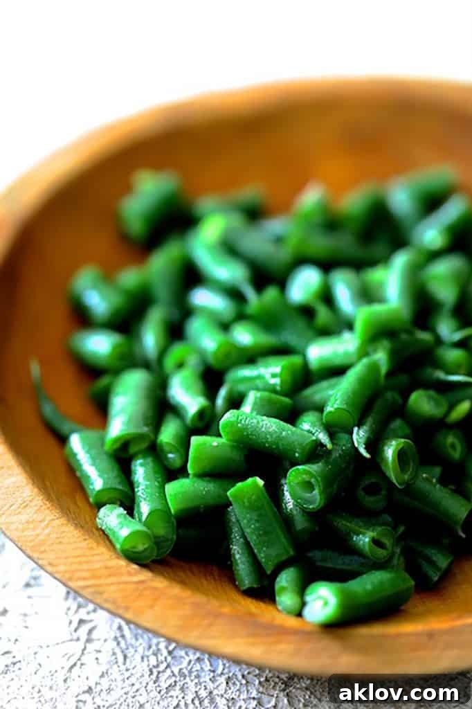 A wooden bowl filled with freshly cooked and vibrant green beans, ready for use in the lasagna.
