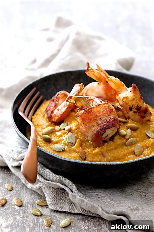 Golden Pumpkin Grits and Crispy Bacon Shrimp 2 Photo of Pumpkin Chipotle and White Cheddar Grits with Bacon Wrapped Shrimp in black bowl on gray napkin garnished with pumpkin seeds, ready to be served.