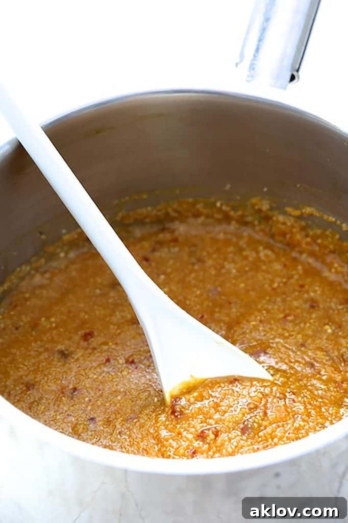 Golden Pumpkin Grits and Crispy Bacon Shrimp 5 Photo of pumpkin grits being stirred with a white spoon in a stainless steel saucepan, showing its creamy texture.